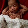 baby, sleeping, blanket, red_background, cozy, infant, peaceful, soft_texture, child, cute, resting, warm, comfort, portrait, indoors, newborn, clothing, relaxed, face, hands_behind_head