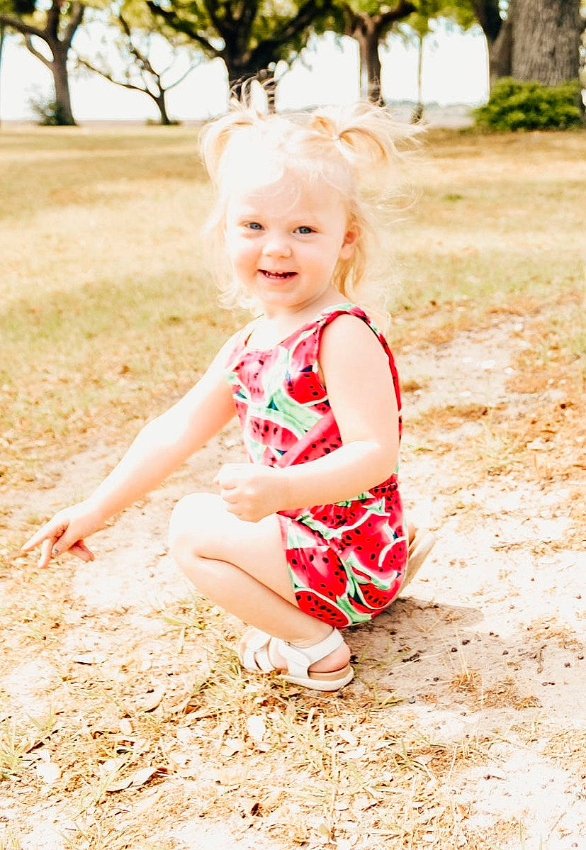 Ruby is registered to the contest to win money with this photo: baby_toddler_clothing, dress, flash_photography, fun, grass, hand, happy, human_leg, leaf, leg, leisure, people_in_nature, person, plant, smile, standing, summer, sunlight, tints_and_shades, toddler