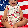 toddler, child, smiling, american_flag, blanket, sitting, indoors, leather_couch, patriotic, clothing, happy, face, person, portrait, feet, hands, home, furniture, cute, background