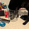 Prettygirl is registered to the contest to win money with this photo: animal, black_cat, black_fur, bottle, claw, cluttered_surface, comb, countertop, curious_cat, domestic_cat, glass_jar, household_items, indoor, papers, pens, pet, soda_can, spray_bottle, stationery, table