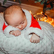 Jaxson joined the competition — help win amazing prizes! baby, sleeping, santa_outfit, christmas_tree, fairy_lights, cushion, holiday, cozy, infant, red_clothing, white_fabric, festive, cute, indoors, decorations, soft_texture, peaceful, child, christmas, newborn