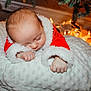 baby, sleeping, santa_outfit, christmas_tree, fairy_lights, cushion, holiday, cozy, infant, red_clothing, white_fabric, festive, cute, indoors, decorations, soft_texture, peaceful, child, christmas, newborn