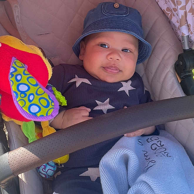 Alijah is registered to the contest to win money with this photo: baby, baby_accessory, baby_blanket, baby_clothing, baby_toy, blanket, blue_outfit, child, comfort, cute, denim_hat, hat, indoors, infant, plush_toy, portrait, seated, smiling, stars, stroller