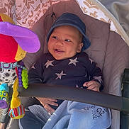 Alijah is registered to the contest to win money with this photo: baby, smiling, stroller, hat, toy, blanket, clothing, child, cute, infant, happy, indoor, seat, fabric, colorful, pattern, playful, comfort, babywear, portrait