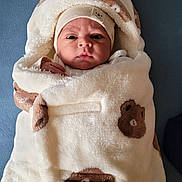 Noah participe au concours pour gagner de l'argent avec cette photo : baby, blanket, bear_pattern, hat, face, infant, wrapped, cozy, soft_texture, cute, child, portrait, warm, snug, clothing, indoor, blue_background, newborn, expression, headwear