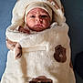 baby, blanket, bear_pattern, hat, face, infant, wrapped, cozy, soft_texture, cute, child, portrait, warm, snug, clothing, indoor, blue_background, newborn, expression, headwear
