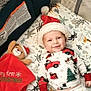 animal_print, baby, bedding, blanket, child, christmas_pajamas, crib, cute, face, festive, holiday, indoors, infant, red, santa_hat, sleeping_area, smiling, teddy_bear, toy, white