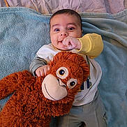 Izaak participe au concours pour gagner de l'argent avec cette photo : baby, blanket, bright_colors, casual_clothing, child, comfort, cozy, cute, hand_in_mouth, happy, indoors, infant, large_toy, laying_down, monkey_toy, playful, plush_toy, smiling, soft_toy, toddler
