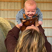 Cole is registered to the contest to win money with this photo: baby, child, person, smiling, overalls, checkered_shirt, hair, barn, hay_bales, sweater, lifting, happy, indoor, portrait, holding, young_child, cute, playful, caucasian, fun