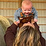 baby, child, person, smiling, overalls, checkered_shirt, hair, barn, hay_bales, sweater, lifting, happy, indoor, portrait, holding, young_child, cute, playful, caucasian, fun
