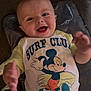 baby, smiling, mickey_mouse, surf_club, shirt, clothing, infant, happy, child, person, cute, lying_down, carpet, hand, face, head, indoor, playful, young_child, apparel