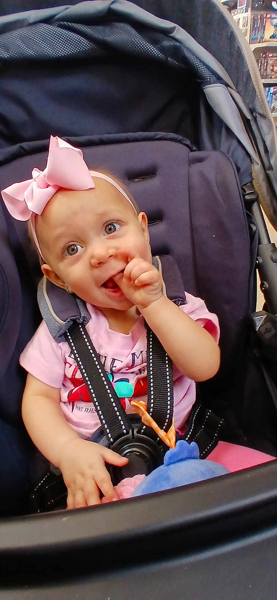 Thyra Eddy Dawn Loza is registered to the contest to win money with this photo: baby, child, stroller, pink_bow, pink_shirt, sucking_thumb, harness, toy, indoor, cute, smiling, face, headband, infant, seated, happy, person, closeup, small_child, playful