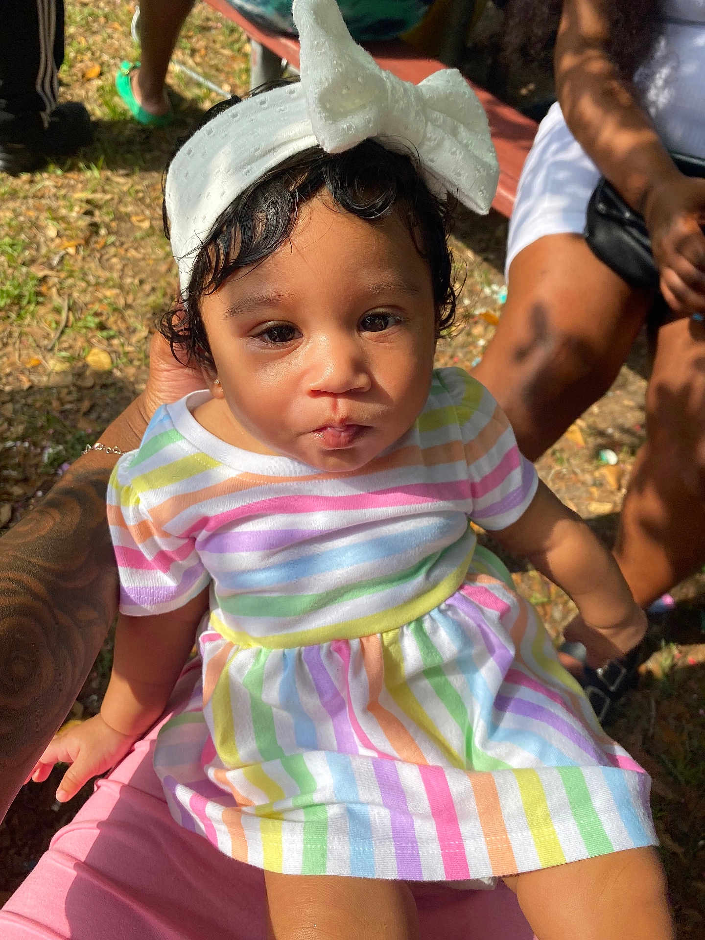 Mylonni is registered to the contest to win money with this photo: toddler, child, baby, outdoor, colorful_clothing, striped_dress, headband, white_bow, person, skin, hair, hand, lap, sunlight, grass, people, legs, footwear, tattoo, casual