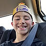 Eli is registered to the contest to win money with this photo:  안전, backseat, birthday_hat, black_shirt, car, child, close_up, crown, face, freckles, happy, indoors, portrait, seatbelt, selfie, smiling, sunlight, teeth, vehicle, window