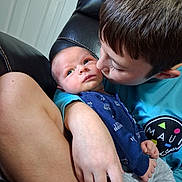 Korbyn joined the competition — help win amazing prizes! baby, infant, child, adult, parent, family, portrait, close_up, cuddle, kiss, affection, smiling, indoor, chair, seated, blue_shirt, onesie, gray_pants, brown_hair, door