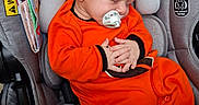 Korbyn is registered to the contest to win money with this photo: baby, infant, sleeping, pacifier, car_seat, orange_outfit, child, portrait, indoors, safety, harness, seated, closed_eyes, peaceful, transportation, automobile, headrest, blanket, warning_label, side_impact_tested