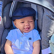 Jules a rejoint le concours — aidez-le/la à gagner de superbes lots ! baby, child, car_seat, cap, white_shirt, blue_shorts, tongue_out, winking, smiling, cute, infant, seat_belt, fabric, clothing, indoors, comfort, playful, portrait, person, young_child