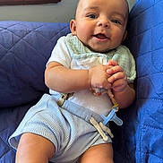 Christian joined the competition — help win amazing prizes! baby, infant, smiling, blue_shorts, white_shirt, pacifier, bib, quilted_couch, indoor, happy, child, clothing, person, sitting, cute, small_hands, face, head, portrait, comfort