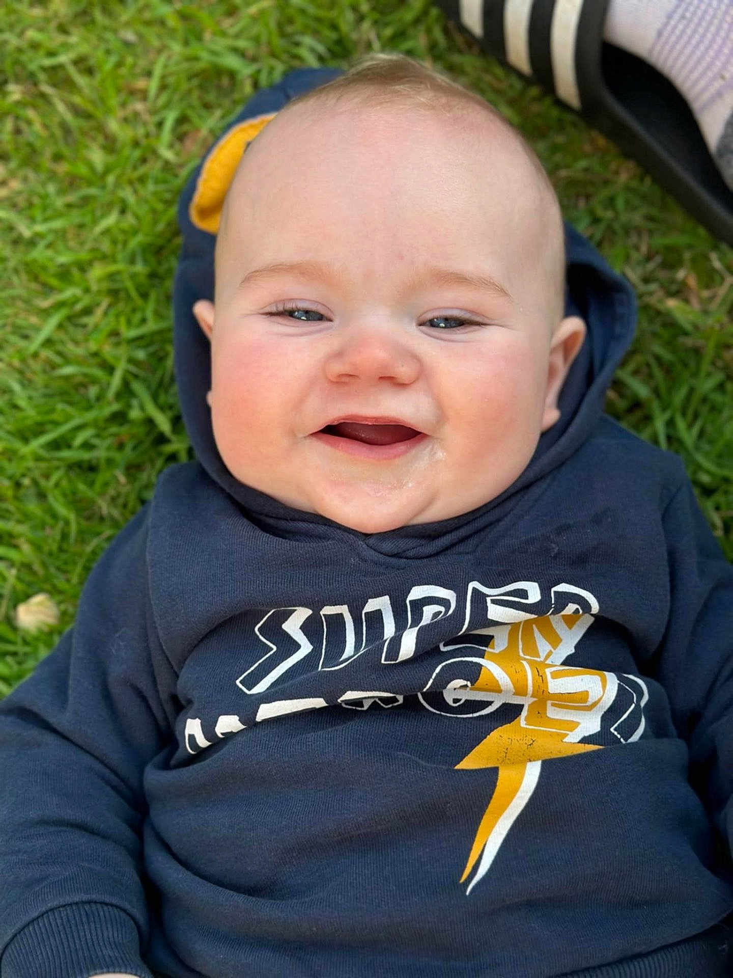 Elio a rejoint le concours — aidez-le/la à gagner de superbes lots ! baby, child, smiling, hoodie, clothing, grass, outdoor, face, happy, infant, portrait, drool, casual, young, cute, person, head, blue, lightning_bolt, expression