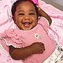 baby, smiling, pink_bow, pink_clothing, blanket, happy, cute, infant, portrait, child, face, hand, curly_hair, cozy, soft_texture, lying_down, indoors, cheerful, ruffled_sleeves, patterned_pants