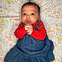 Gianna is registered to the contest to win money with this photo: baby, blanket, child, clasped_hands, close_up, clothing, curious, cute, denim_dress, eyes, floral_background, hair_topknot, indoor, infant, laying_down, portrait, red_sweater, skin, soft_lighting, wide_eyes