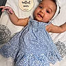 Gianna is registered to the contest to win money with this photo: arm, baby, blanket, bow, celebration, child, cute, dress, face, hand, headband, indoor, infant, lying_down, milestone, portrait, skin, smile, text, wooden_sign