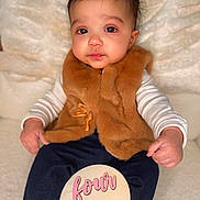 Gianna is registered to the contest to win money with this photo: baby, infant, child, four_months, milestone_sign, wooden_sign, fur_vest, brown_vest, blanket, portrait, indoor, cute, big_eyes, chubby_cheeks, sitting, hands, socks, dark_pants, soft_lighting, close_up