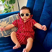 Devansh is registered to the contest to win money with this photo: baby, bare_feet, blue_couch, child, cozy, cushion, cute, fashion, houseplant, indoor, infant, living_room, photograph, portrait, red_outfit, relaxed, seated, smiling, striped_clothing, sunglasses