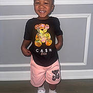 Zyheir is registered to the contest to win money with this photo: black_tshirt, casual_clothing, child, cute, fashion, floor, footwear, happy, indoor, light_skin, person, pink_shorts, playful, portrait, short_hair, smiling, standing, toddler, wall, white_sneakers