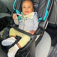 Kyree joined the competition — help win amazing prizes! baby, car_seat, pacifier, infant, child, smiling, clothing, hoodie, shoes, seatbelt, vehicle_interior, car, yellow_pants, gray_jacket, happy, cute, sitting, person, young_child, indoors