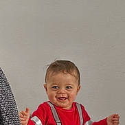 Mylhan participe au concours pour gagner de l'argent avec cette photo : child, baby, smiling, highchair, red_clothing, plain_wall, indoor, couch, upholstery, face, happy, brown_hair, eyes, hands, arms, seat, tray, portrait, cheerful, toddler