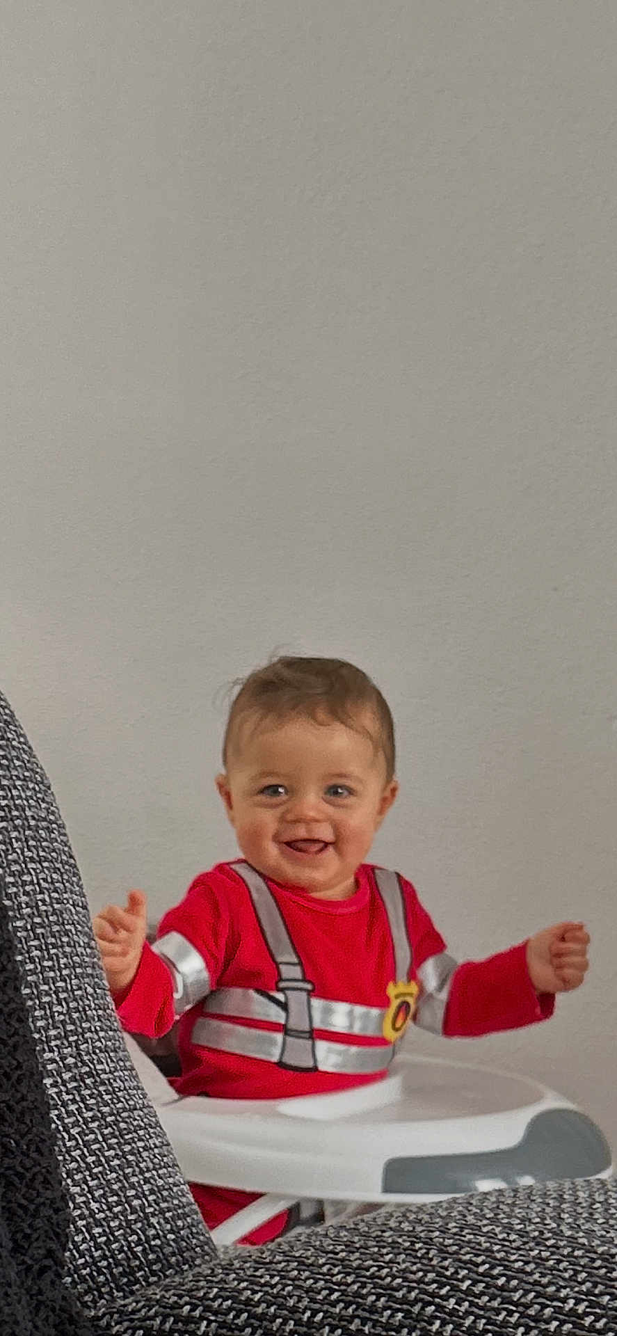 Mylhan participe au concours pour gagner de l'argent avec cette photo : child, baby, smiling, highchair, red_clothing, plain_wall, indoor, couch, upholstery, face, happy, brown_hair, eyes, hands, arms, seat, tray, portrait, cheerful, toddler