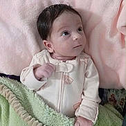 Ausrine is registered to the contest to win money with this photo: baby, infant, child, portrait, indoors, nursery, blanket, pink_blanket, green_blanket, floral_background, baby_clothing, onesie, sitting, lying_down, wide_eyes, dark_hair, cozy, soft_furnishings, natural_light, close_up