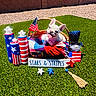 dog, french_bulldog, puppy, basket, american_flag, patriotic, stars_and_stripes, blanket, grass, outdoor, sunlight, decorations, red, white, blue, star, smiling, tongue_out, summer, celebration