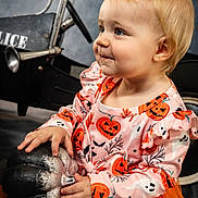 Isabelle is registered to the contest to win money with this photo: toddler, child, halloween, pumpkin, dress, orange, ghost, jack_o_lantern, toy_car, police, vintage, portrait, smile, cute, costume, indoor, face, hands, blue_eyes, blonde_hair