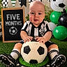 Lucas joined the competition — help win amazing prizes! baby, soccer_ball, cake, chalkboard, balloons, grass, sportswear, celebration, birthday, milestone, black_and_white, striped_clothing, socks, shoes, decorations, indoor, portrait, smiling, child, hands