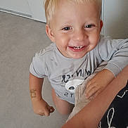 Luka a rejoint le concours — aidez-le/la à gagner de superbes lots ! child, toddler, blonde_hair, smiling, indoor, floor, gray_floor, sandal, hand, arm, shirt, tattoo, person, happy, looking_up, short_sleeves, casual_clothing, skin, face, standing