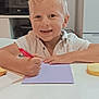 child, boy, smiling, drawing, pen, paper, table, kitchen, bread, blonde_hair, white_shirt, appliance, microwave, shelf, container, indoor, food, happy, casual_clothing, person