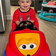 Hayden is registered to the contest to win money with this photo: toddler, child, toy_car, red_shirt, spiderman, smiling, indoor, living_room, couch, floor, plastic_toy, happy, cute, person, furniture, play, young_child, vehicle, head, seat