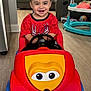 toddler, child, toy_car, red_shirt, spiderman, smiling, indoor, living_room, couch, floor, plastic_toy, happy, cute, person, furniture, play, young_child, vehicle, head, seat