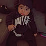 baby, child, hoodie, nike, black_clothing, socks, striped_socks, couch, indoor, plush_toy, toy_phone, person, seated, curious_expression, young_child, casual_wear, soft_lighting, cozy, infant, portrait