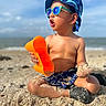 bare_chest, beach, bucket_hat, child, footwear, hat, ocean, orange, outdoor, play, sand, sand_on_skin, shorts, summer, sunglasses, sunny, toddler, toy, vacation, water