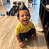 barefoot, candid, child, dinosaur_shirt, expression, flooring, hair_spike, happy, indoor, playing, portrait, room, shelf, smile, sneaker, stroller, toddler, toy, wooden_floor, yellow_shirt