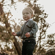 Martin participe au concours pour gagner de l'argent avec cette photo : bokeh, casual_clothing, child, curious, cute, daylight, exploration, forest, innocence, nature, outdoor, pants, portrait, rock, standing, sunlight, sweater, toddler, trees, young_child