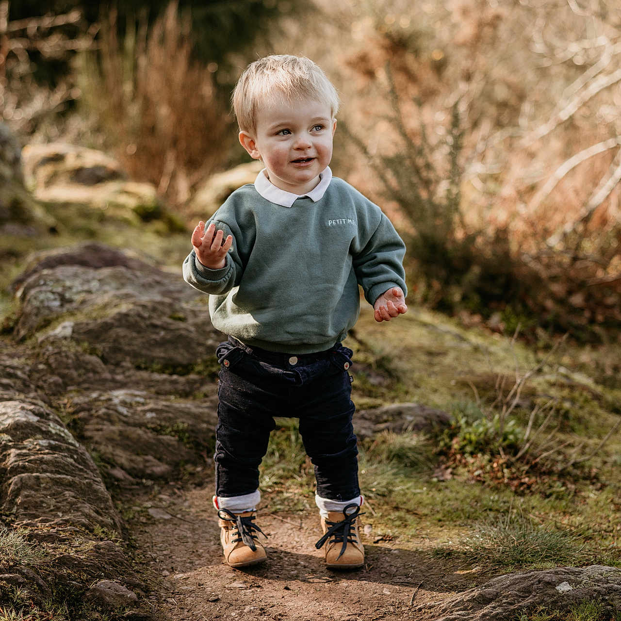 Martin participe au concours pour gagner de l'argent avec cette photo : adventure, boots, casual_clothing, child, curly_hair, daytime, exploring, forest, green_sweatshirt, happy, nature, outdoor, path, rocks, smile, sunlight, toddler, trees, walking, young
