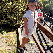 Leevay participe au concours pour gagner de l'argent avec cette photo : child, boy, outdoor, sunlight, greenery, soda_bottle, cap, white_clothing, black_sneakers, curb, sidewalk, wooden_railings, shadow, summer, casual, young, standing, nature, playful, daytime