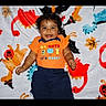 Matheo joined the competition — help win amazing prizes! baby, child, infant, smiling, happy, portrait, lying_down, indoor, halloween, blanket, orange_shirt, dark_pants, clothing, face, eyes, hair, hands, text_on_clothing, colorful, photography