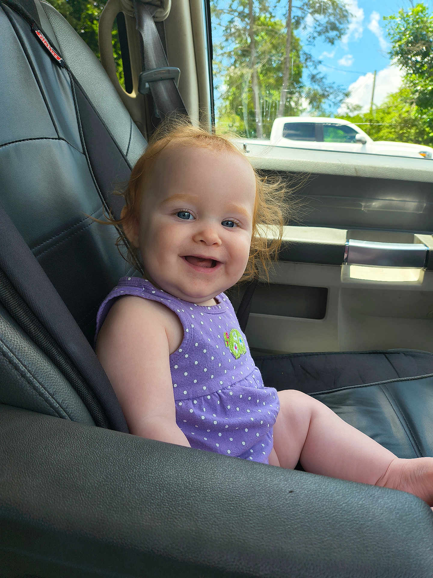 Brennley is registered to the contest to win money with this photo: baby, child, smile, car_seat, purple_clothing, polka_dot, red_hair, blue_eyes, vehicle_interior, window, sunlight, trees, outdoor, happy, portrait, infant, seatbelt, skin, person, daytime