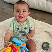Peter joined the competition — help win amazing prizes! baby, child, smiling, toy, plush_toy, quilt, indoor, floor, happy, cute, clothing, sitting, face, person, home, teething_toy, infant, short_sleeve, sock, wooden_floor