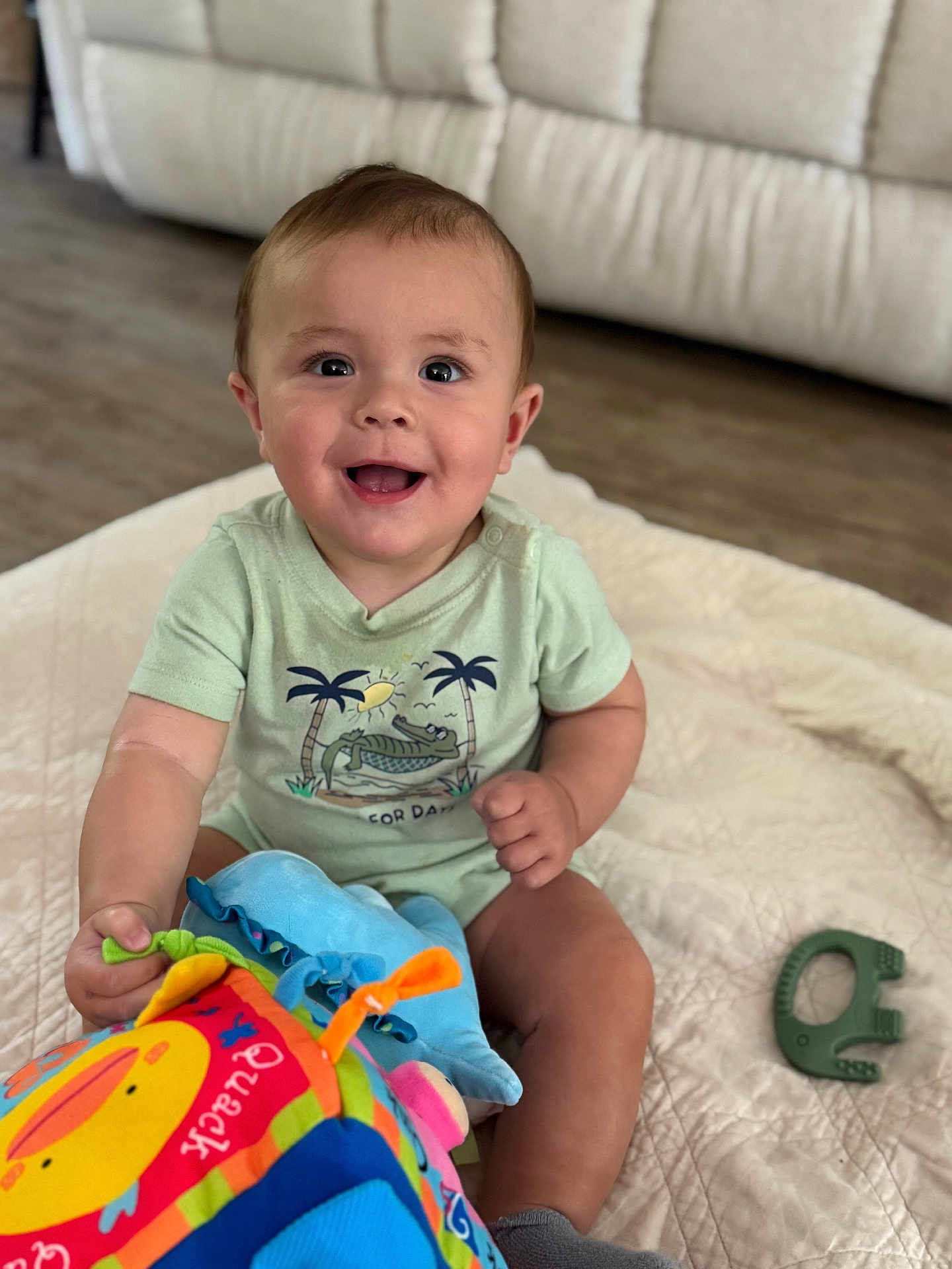 Peter joined the competition — help win amazing prizes! baby, child, smiling, toy, plush_toy, quilt, indoor, floor, happy, cute, clothing, sitting, face, person, home, teething_toy, infant, short_sleeve, sock, wooden_floor